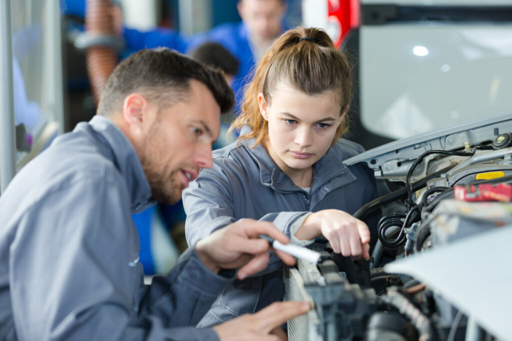 Apprentie mécanicienne formée par un technicien expérimenté sur un moteur dans un garage automobile