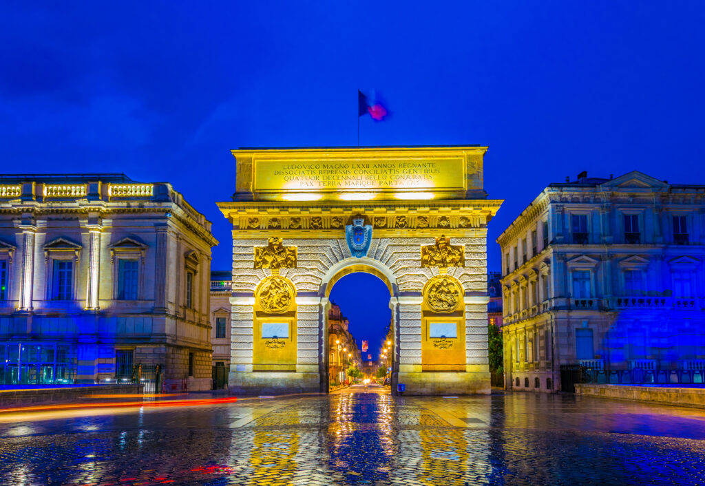 Arc de Triomphe de la Porte du Peyrou illuminé de nuit avec reflets sur les pavés mouillés à Montpellier