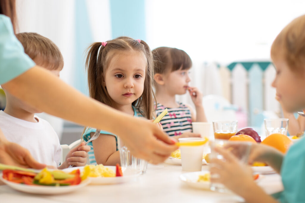 Enfants attablés à la cantine scolaire partageant un repas équilibré avec fruits et légumes
